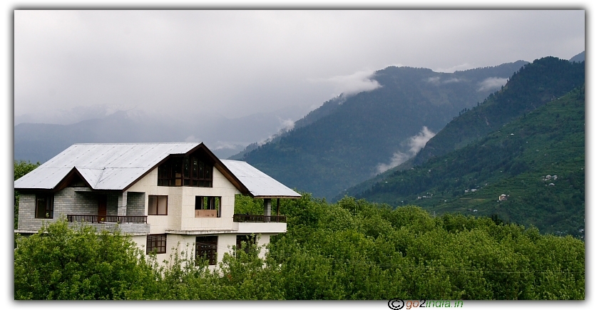 Ice peaks, clouds, green land and house at Khakhnal, Manali