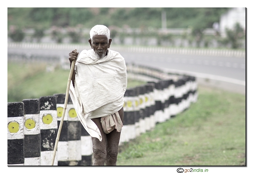 old aged villager walking alone beside the road