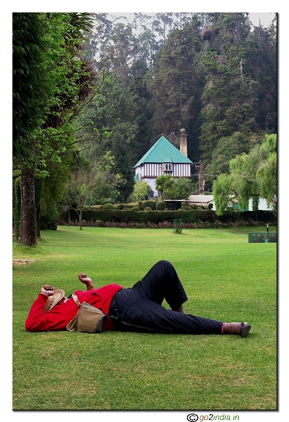 Person taking rest on the green grass lawn at Botanical garden of Ooty