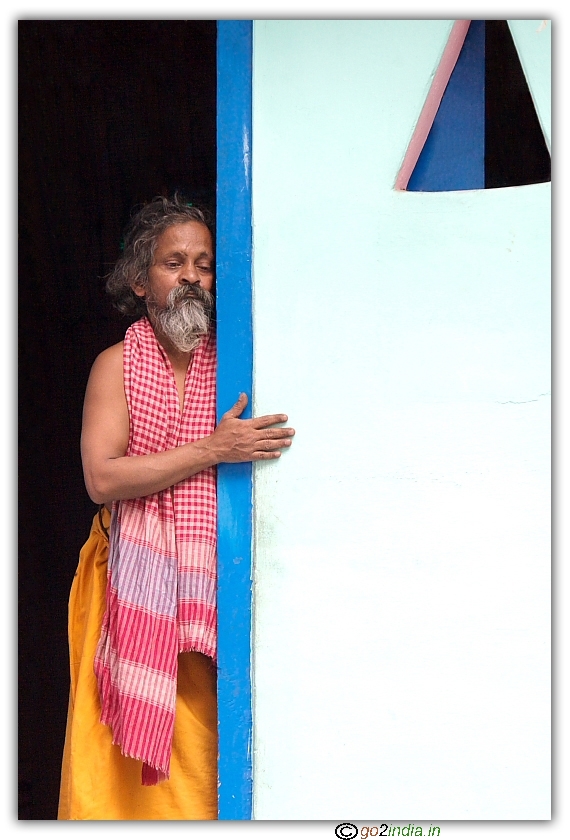 man leaning to wall and seeing people doing puja at Shiva temple, Manikaran